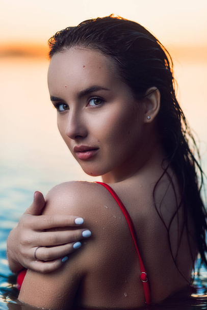 Portrait of a beautiful woman with wet hair in a sexy red bikini against the backdrop of the sea and sunset. fashionable stylish young woman on tropical beach - Photo, Image