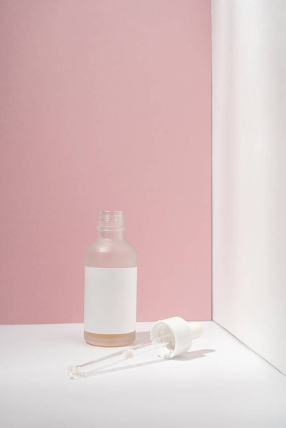 Cosmetic bottle with an eyedropper on a white-pink background. - Фото, изображение
