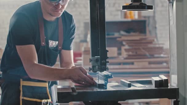 Hombre en un taller de carpintería cortando piezas del detalle de madera usando una máquina de corte estática - Metraje, vídeo