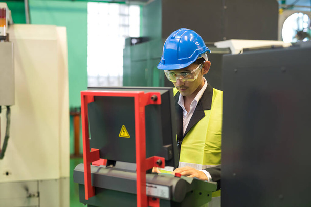 Waist up warehouse manager with hardhat and protection glasses command computer to produce mechanic microchip part by automate CNC lache robot machine in factory workshop. - 写真・画像