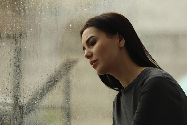 Depressed woman near window on rainy day, space for text - Фото, зображення