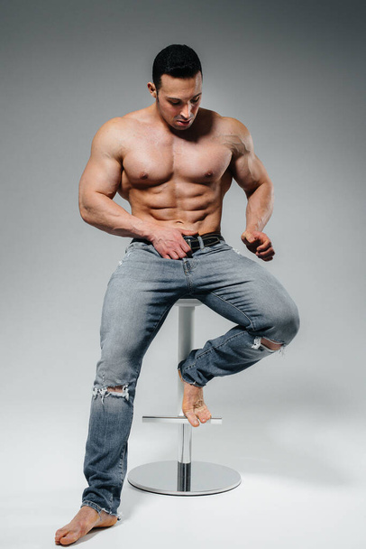 A young athlete in jeans poses sitting in the studio. Sport. - Фото, зображення