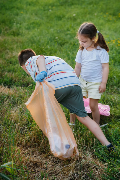 A group of girls with children at sunset are engaged in garbage collection in the park. Environmental care, recycling. - Foto, Imagen