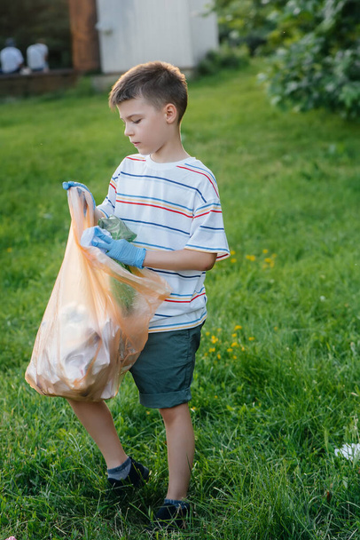 A seven-year-old boy at sunset is engaged in garbage collection in the park. Environmental care, recycling. - Foto, Imagen