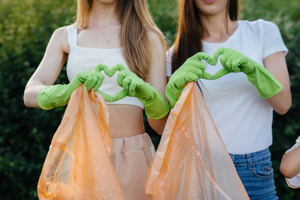 A group of young women with children show hearts after cleaning garbage in the park during sunset. Environmental care, recycling. - Photo, Image