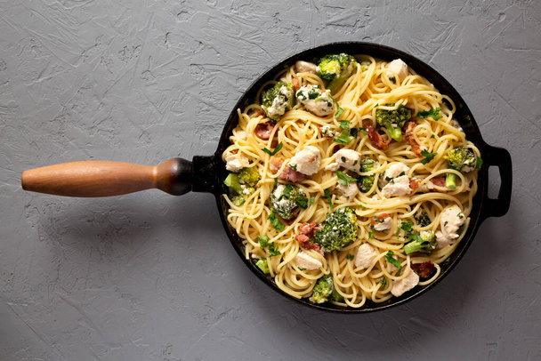 Homemade Chicken Bacon Broccoli Alfredo in a cast-iron pan on a gray surface, top view. Flat lay, overhead, from above. - Zdjęcie, obraz