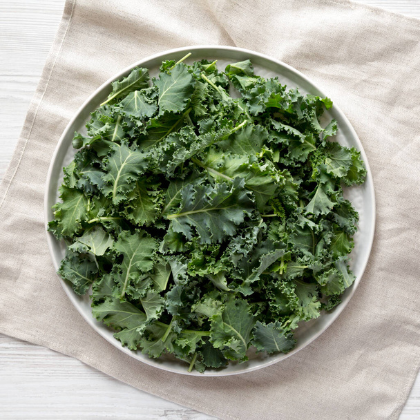 Raw Organic Baby Kale on a gray plate on a white wooden background, top view. Flat lay, overhead, from above.  - Foto, immagini