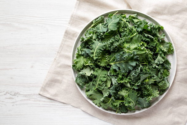 Raw Organic Baby Kale on a gray plate on a white wooden surface, top view. Flat lay, overhead, from above. Copy space. - Photo, image