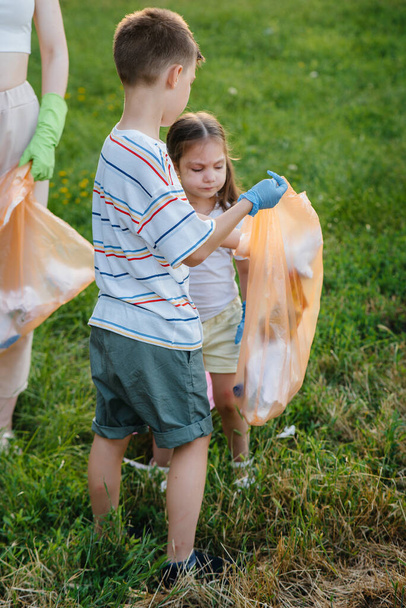 Un gruppo di ragazze con bambini al tramonto sono impegnati nella raccolta dei rifiuti nel parco. Protezione dell'ambiente, riciclaggio. - Foto, immagini