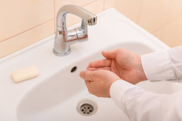 kézmosás szappannal vagy géllel folyó víz alatt a mosdókagylóban, tisztaság és higiénia, férfi kéz fehér ingben - Fotó, kép