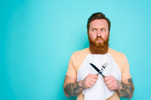 Чоловік з татуюваннями готовий їсти з столовими приборами в руці з деякими сумнівами
 - Фото, зображення