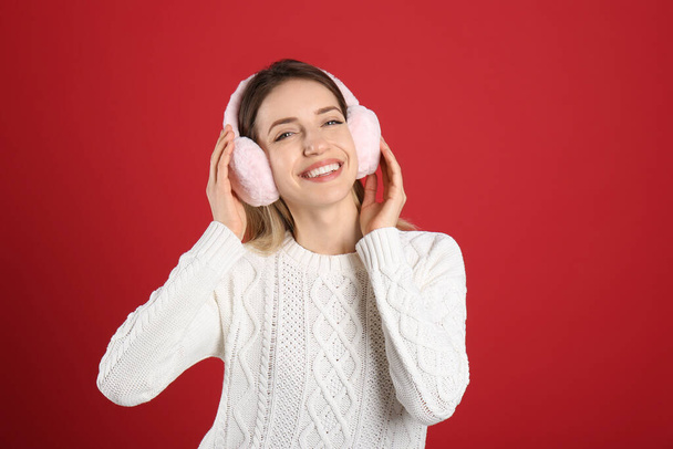 Happy woman wearing warm earmuffs on red background - Фото, изображение