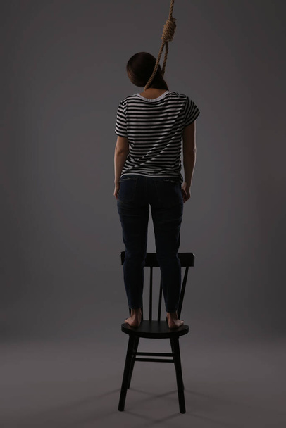 Woman with rope noose standing on chair against grey background, back view - Photo, image
