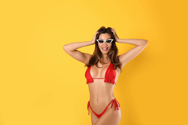 Beautiful woman in stylish bikini and sunglasses on yellow background - Фото, зображення