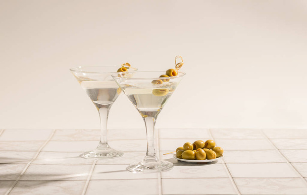 Martini koktajl z oliwkami na stole z kafelkami. Klasyczny napój alkoholowy z lodem w eleganckiej szklance - Zdjęcie, obraz