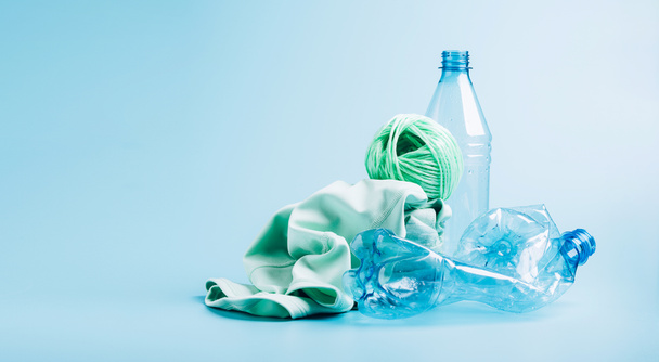 Prázdné plastové láhve a různé tkaniny z recyklovaných polyesterových vláken syntetické tkaniny na modrém pozadí - Fotografie, Obrázek