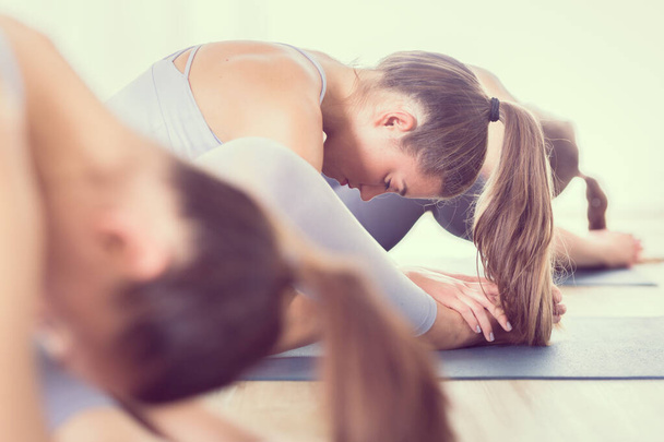 Gruppo di giovani donne attraenti sportive in studio di yoga, praticare lezione di yoga con istruttore, seduto sul pavimento in avanti piegare yoga sana postura. Stile di vita attivo sano, allenarsi al chiuso in palestra - Foto, immagini