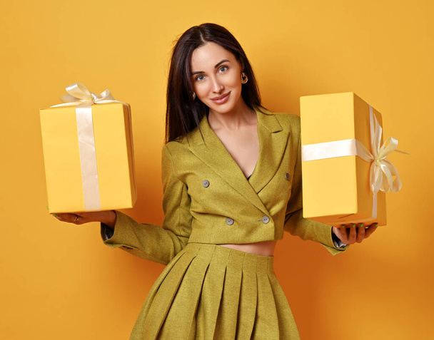 Beautiful smiling young brunette woman in yellow costume skirt and jacket standing holding present boxes looking at camera - Zdjęcie, obraz