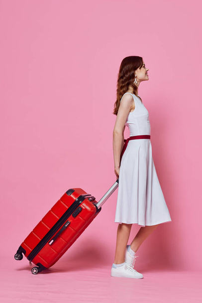 nainen punainen matkalaukku valkoinen mekko tunteet matkustaa vaaleanpunainen tausta - Valokuva, kuva
