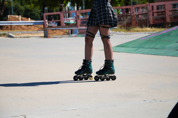 young and beautiful girl with punk and heavy tendency skating in the skating rink. The girl is wearing fishnet stockings and a plaid skirt with inline skates. - Photo, Image