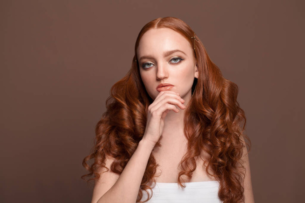 Atrakcyjny rudowłosy model o zdrowej skórze i długich rudych włosach na brązowym tle - Zdjęcie, obraz
