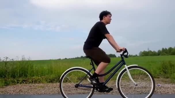 Young man alone riding bicycle on road at countryside on field, forest background. Summer activity, healthy lifestyle, workout, sport, fitness. Alone person in nature. Having fun outdoors. - Footage, Video
