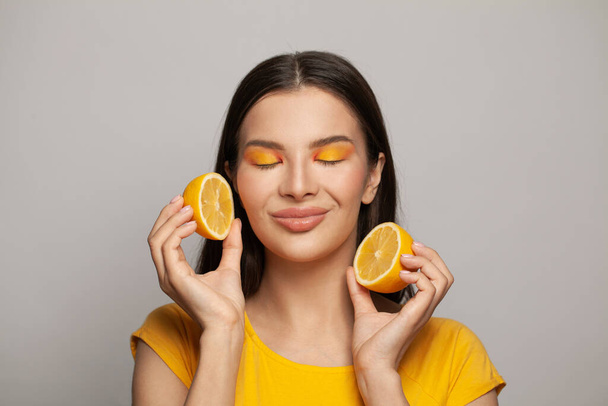 Cute brunette woman holding yellow lemon fruits on white background - Фото, изображение