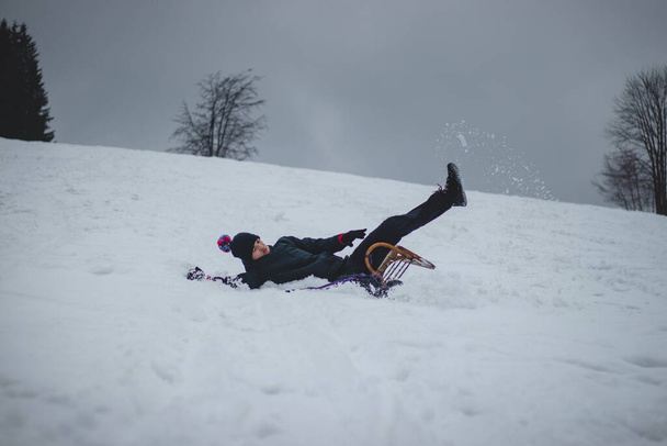 Athlet stürzt vom Holzschlitten und fällt schwer auf den Schnee und breitet sich aus. Der Schlitten des Jungen blieb stecken, warf ihn hinaus und er machte einen Salto. Harte Landung auf der Piste. Gefährlicher Sturz. - Foto, Bild