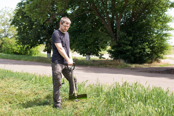 Человек с электрической газонокосилкой стрижет траву. Для магазина садового оборудования с местом для текста. - Фото, изображение