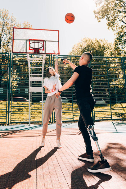 Молодой человек с протезной ногой играет в баскетбол со своим другом на корте - Фото, изображение
