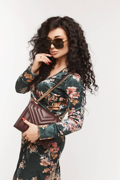 Portrait of a model woman with curly hair in trendy dress and sunglasses with modish purse isolated on the white background. - Foto, imagen