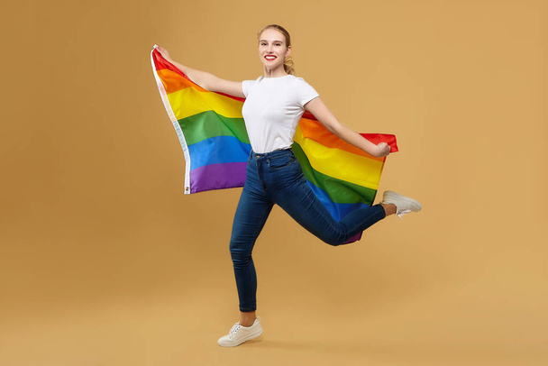 attractive blonde made a jump with a rainbow LGBT flag. photo shoot in the studio on a yellow background. - Photo, image