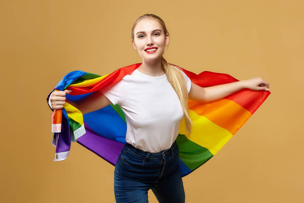 attractive blonde made posing with a rainbow LGBT flag. photo shoot in the studio on a yellow background. - Φωτογραφία, εικόνα