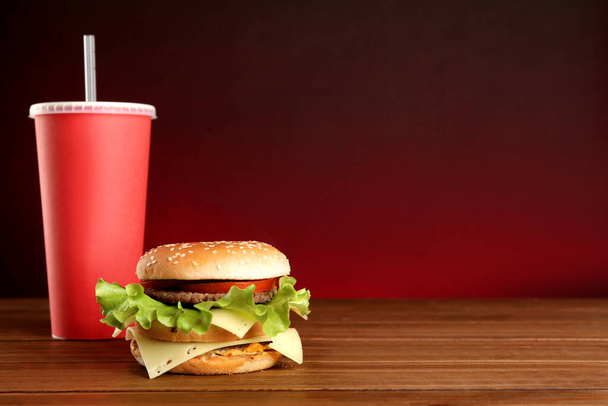Delicious burger and drink on wooden table against red background, space for text. Fast food menu - Φωτογραφία, εικόνα