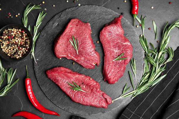 Fresh raw meat steaks and spices on black table, flat lay - Foto, afbeelding