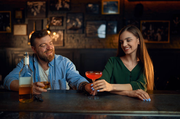 Pariskunta alkoholin kanssa tutustuu tiskillä baarissa. Mies ja nainen juhlia kokousta pubissa, ihmisen tunteita, vapaa-ajan toimintaa, flirttailu - Valokuva, kuva