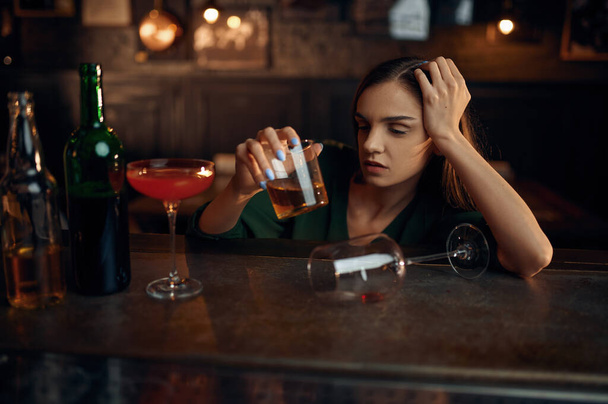 Μεθυσμένη γυναίκα πίνει διαφορετικό αλκοόλ στον πάγκο στο μπαρ. Ένα θηλυκό πρόσωπο σε παμπ, ανθρώπινα συναισθήματα, δραστηριότητες αναψυχής, νυχτερινή ζωή - Φωτογραφία, εικόνα