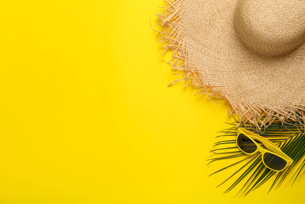 Straw hat, sunglasses, palm leaf and space for text on yellow background, flat lay. Stylish headdress - Foto, Imagen