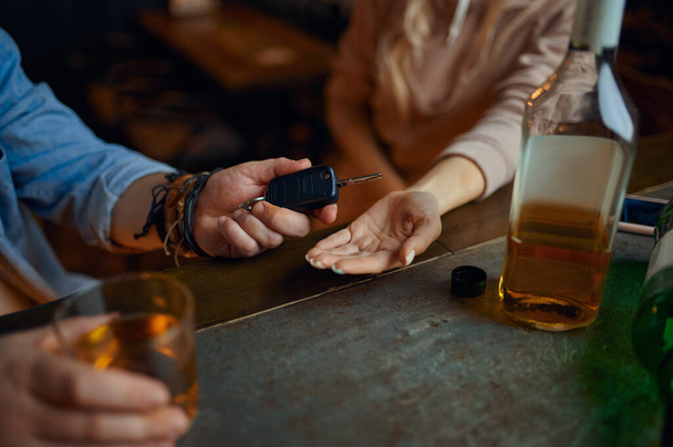 Dronken man geeft de autosleutels aan zijn nuchtere vrouw aan de bar. Man rustend in pub, vrijetijdsbesteding. Een redelijke daad, weigert te rijden onder invloed van alcohol - Foto, afbeelding