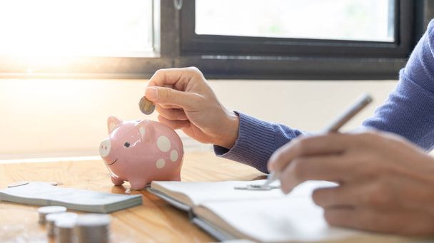 Man puts a coin dollar in a piggy bank, Saving money for future growth and knowing how to manage your spending wisely, Saving money for business growth or long-term profitability. - Foto, Imagen