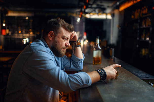 Sad bearded man sitting at the counter in bar. One angry male person in pub, human emotions and leisure activities, depression, stress relief - Valokuva, kuva
