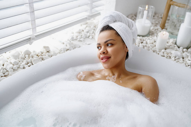 Viettelevä nainen rentoutua vaahtokylvyssä. Nainen kylpyammeessa, kauneus ja terveydenhuolto kylpylässä, wellness-hoito kylpyhuoneessa, pikkukivet ja kynttilät taustalla - Valokuva, kuva