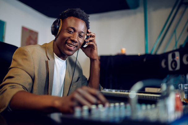 Boldog férfi DJ a fejhallgatóban, stúdió belső tér a háttérben. Szintetizátor és audio mixer, zenész munkahely, kreatív folyamat - Fotó, kép