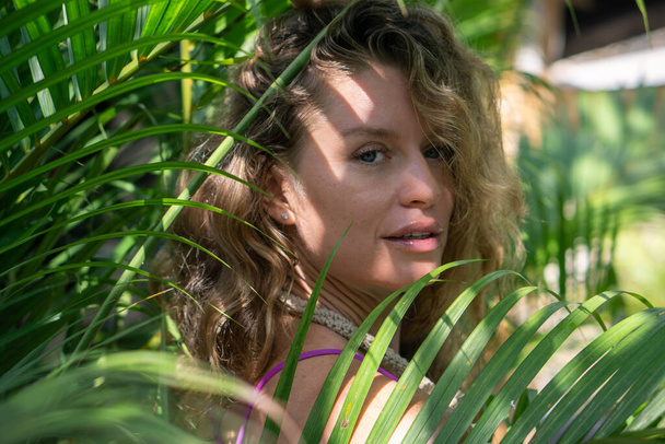 Young woman with curly long blonde hair in tropical green jungle with palm trees in Bali - Φωτογραφία, εικόνα