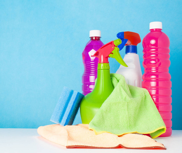Вид на различные чистящие средства с двумя печеньями и губкой для мытья посуды на синем фоне - Фото, изображение