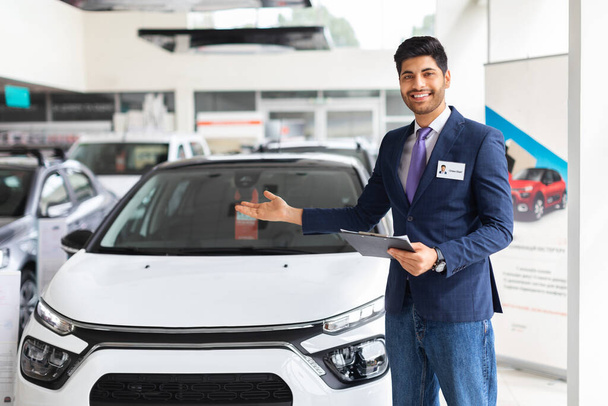 Handsome young salesman standing at the dealership, showing car - Photo, Image