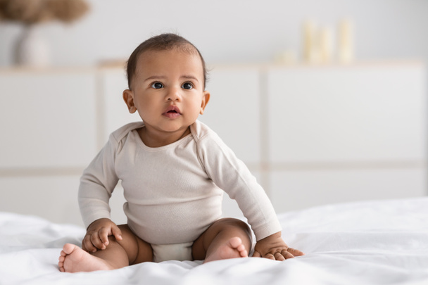 Cute little African American infant sitting on bed - Photo, Image