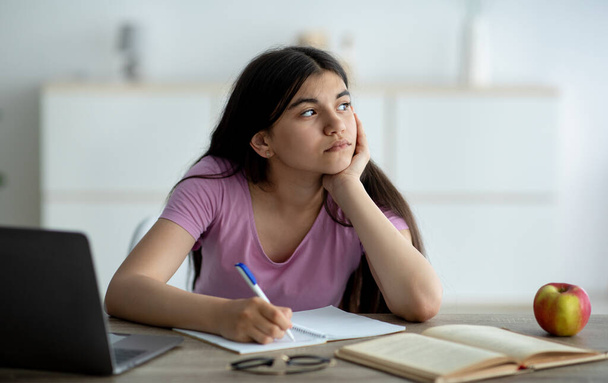 Menina adolescente indiano pensativo estudando on-line a partir de casa, tomando notas durante a lição da web, sentindo-se entediado em casa, panorama - Foto, Imagem
