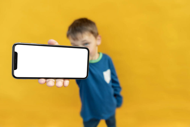 The child holds the phone in his hand for advertising on a yellow background. Color - Fotó, kép