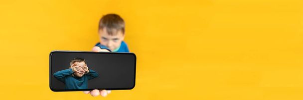 The child holds the phone in his hand for advertising on a yellow background. Color - Foto, Bild